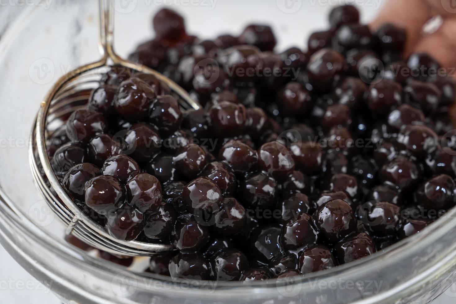 Making bubble tea, scoop and pour cooked brown sugar flavor tapioca pearl bubble balls into cup on white wooden table background, close up, copy space. photo