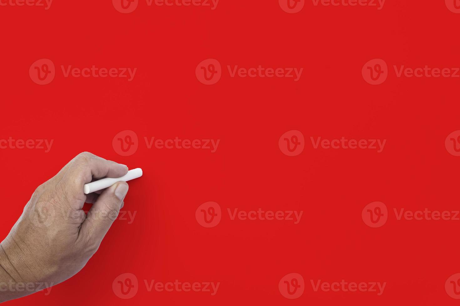 Male hand writes in white chalk pencil on a red background. Copy space. photo