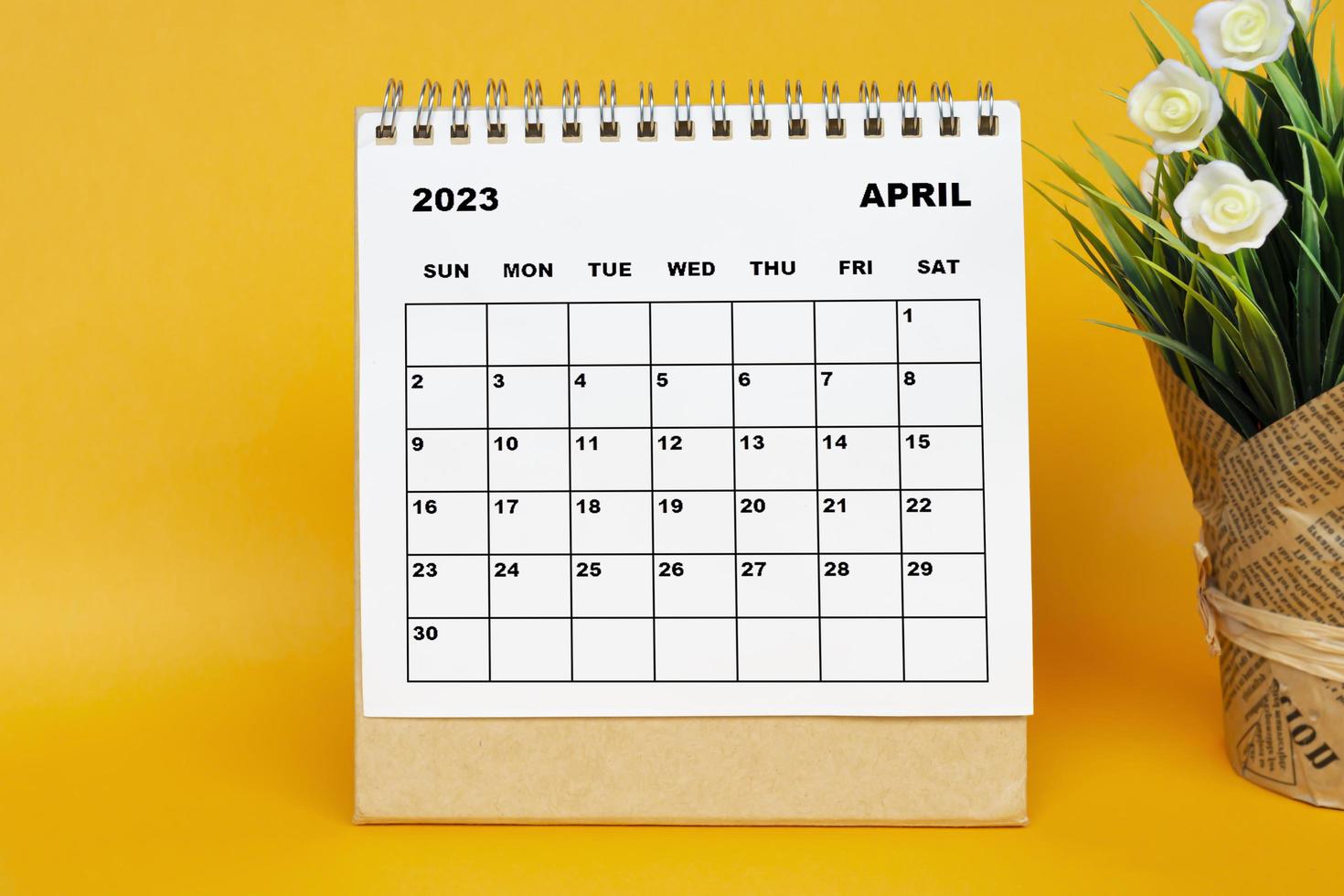 Calendario blanco de abril de 2023 con planta en maceta sobre fondo amarillo. foto