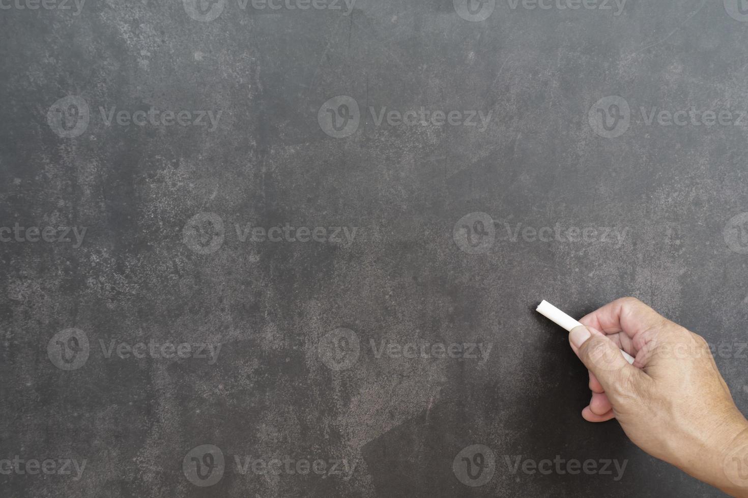 Male hand writes in white chalk pencil on a chalkboard background. Copy space. photo