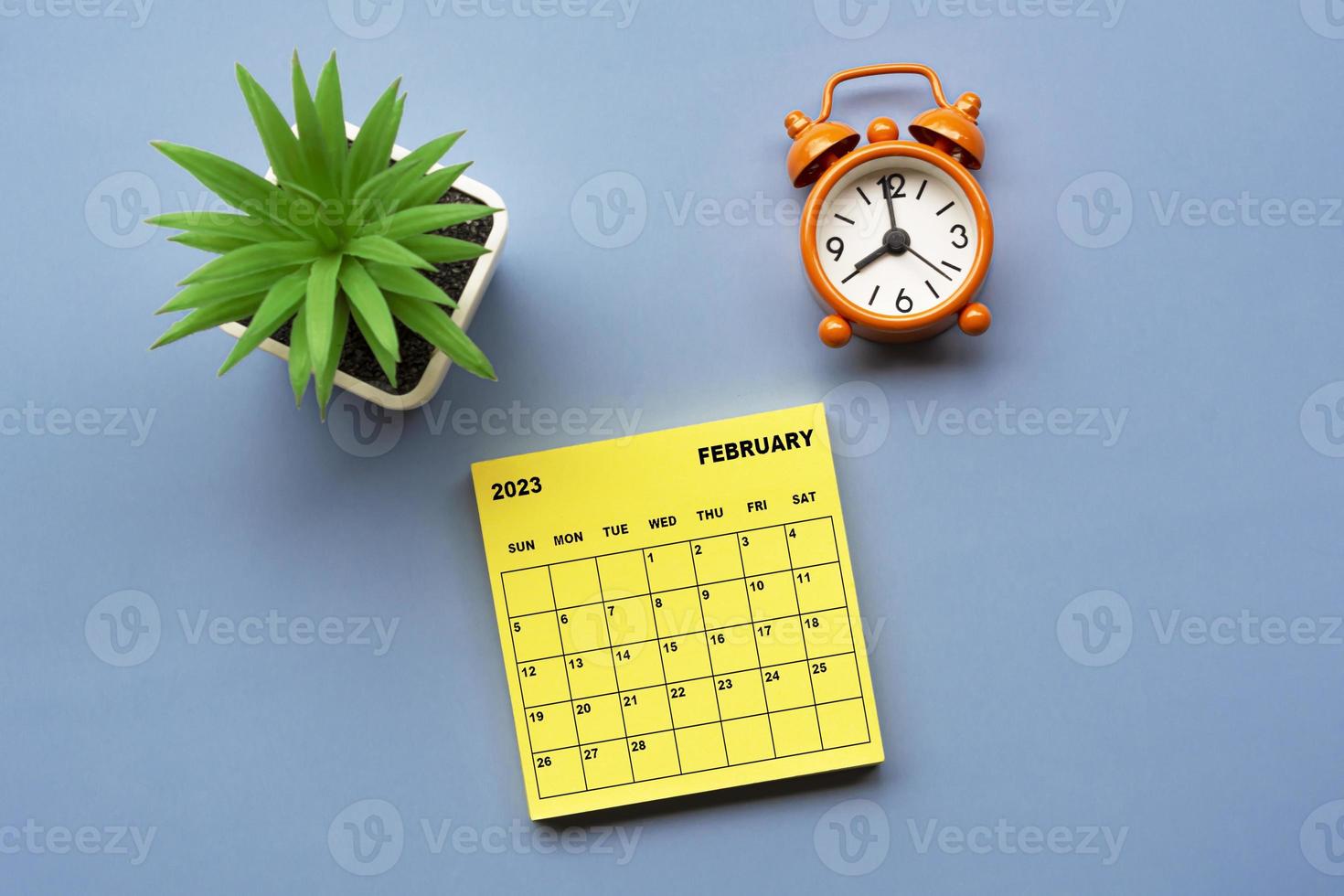 February 2023 calendar on Adhesive Note with alarm clock set at 8 o'clock. photo