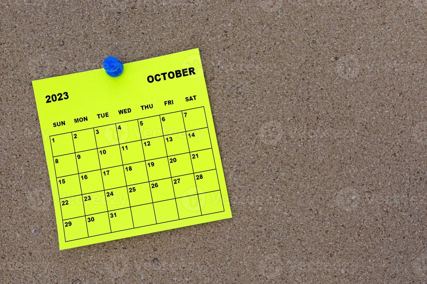 October 2023 yellow sticky note calendar with pin on cork bulletin billboard. photo