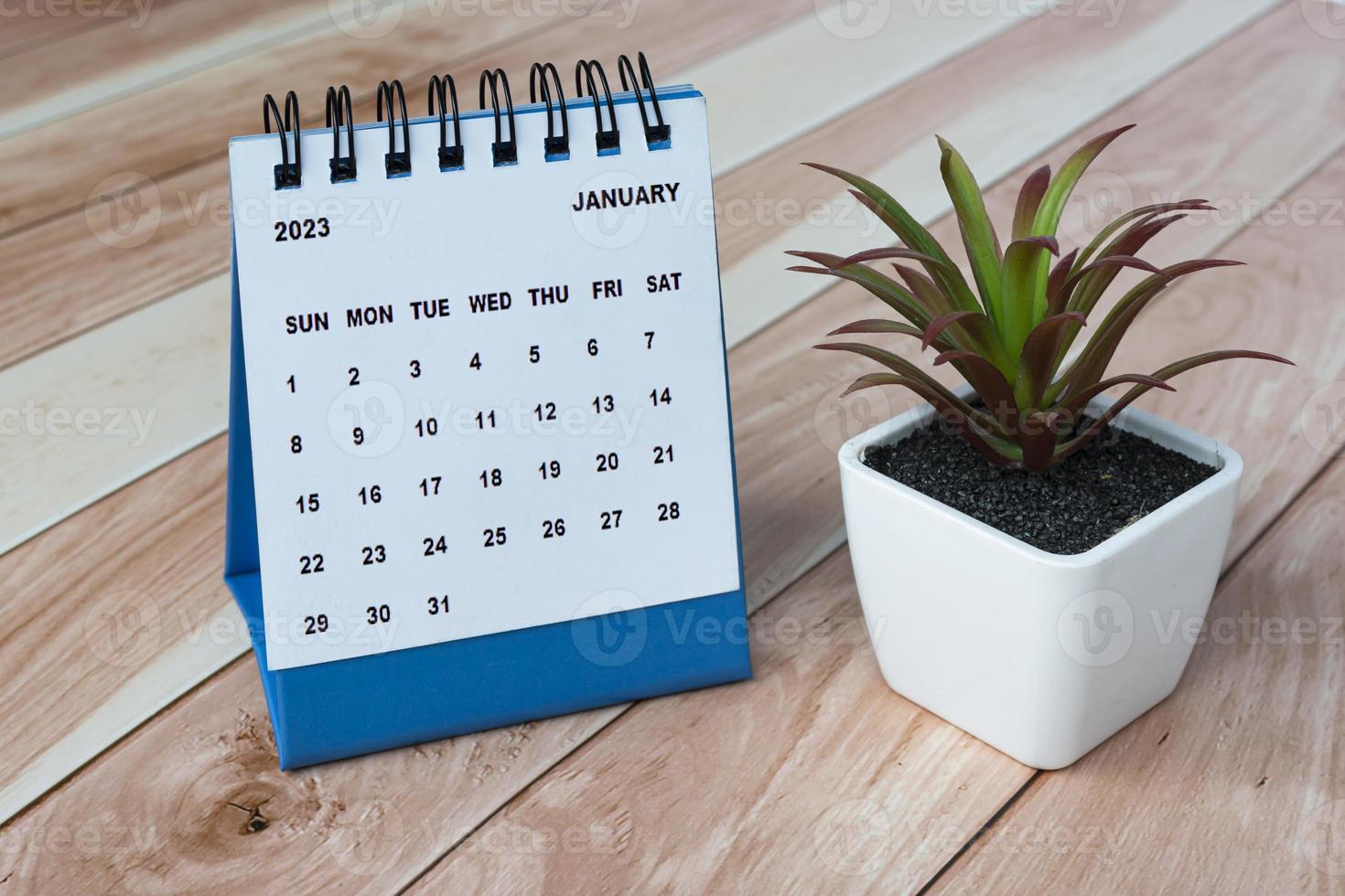 calendario de escritorio de enero de 2023 sobre una mesa de madera con planta en maceta. foto