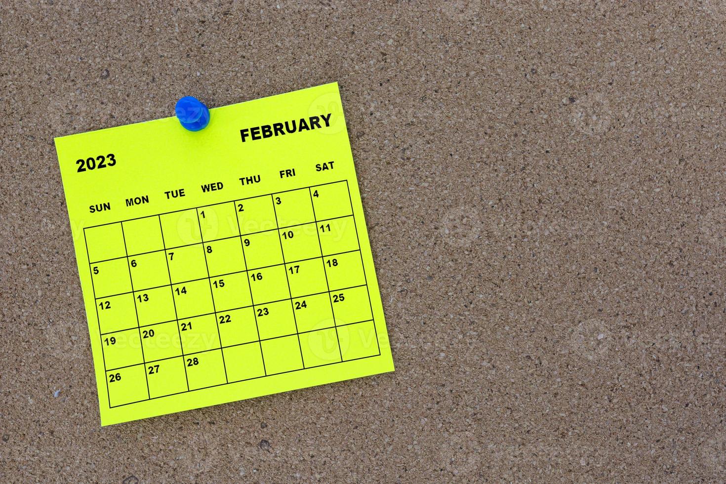 February 2023 yellow sticky note calendar with pin on cork bulletin billboard. photo