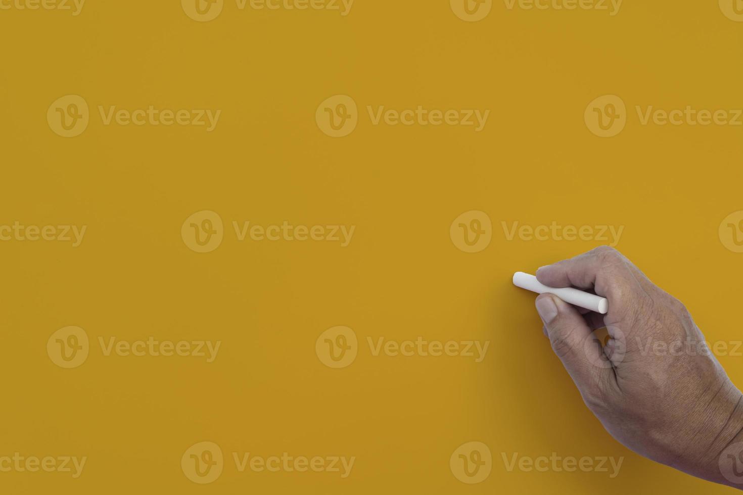 Male hand writes in white chalk pencil on a yellow background. Copy space. Teaching concept.Male hand writes in white chalk pencil on a yellow background. Copy space. photo