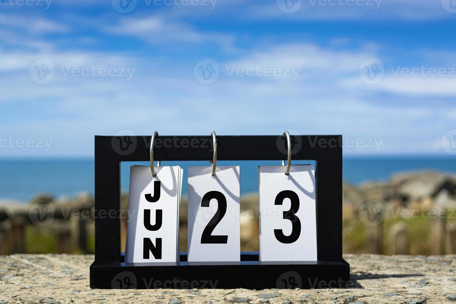 23 de junio texto de fecha de calendario en marco de madera con fondo borroso del océano. foto