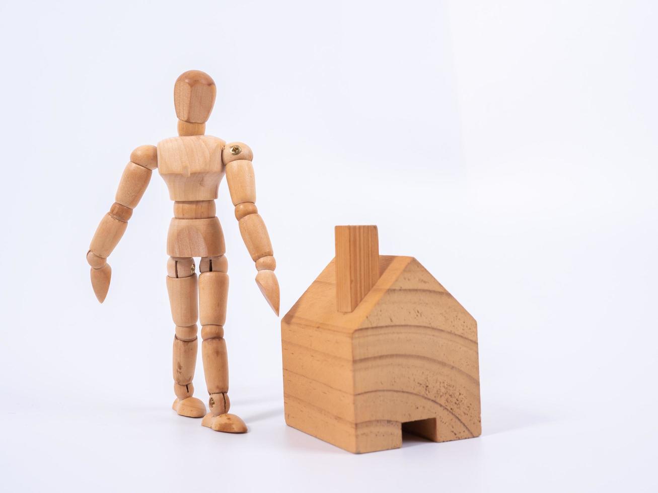 Man leaned against the model of a house isolated on white background. Concept with a wooden puppet photo