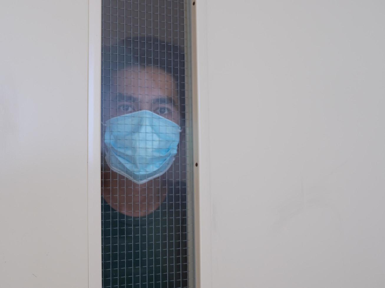 Lonely man in medical mask looking through the window. Isolation at home for self quarantine. Concept home quarantine, prevention COVID-19. Coronavirus outbreak situation photo