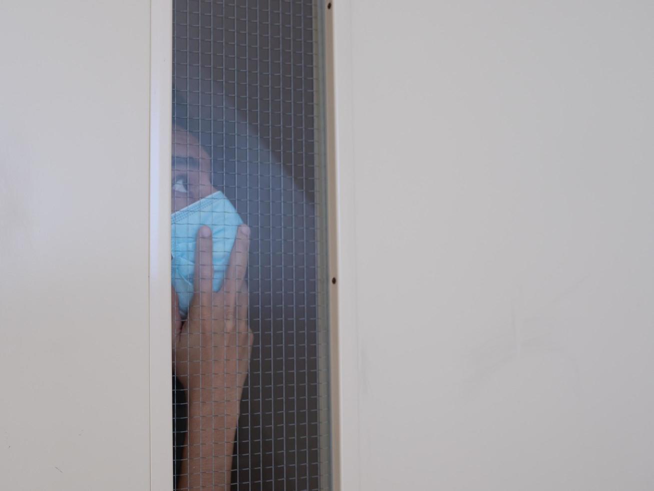 Lonely man in medical mask looking through the window. Isolation at home for self quarantine. Concept home quarantine, prevention COVID-19. Coronavirus outbreak situation photo