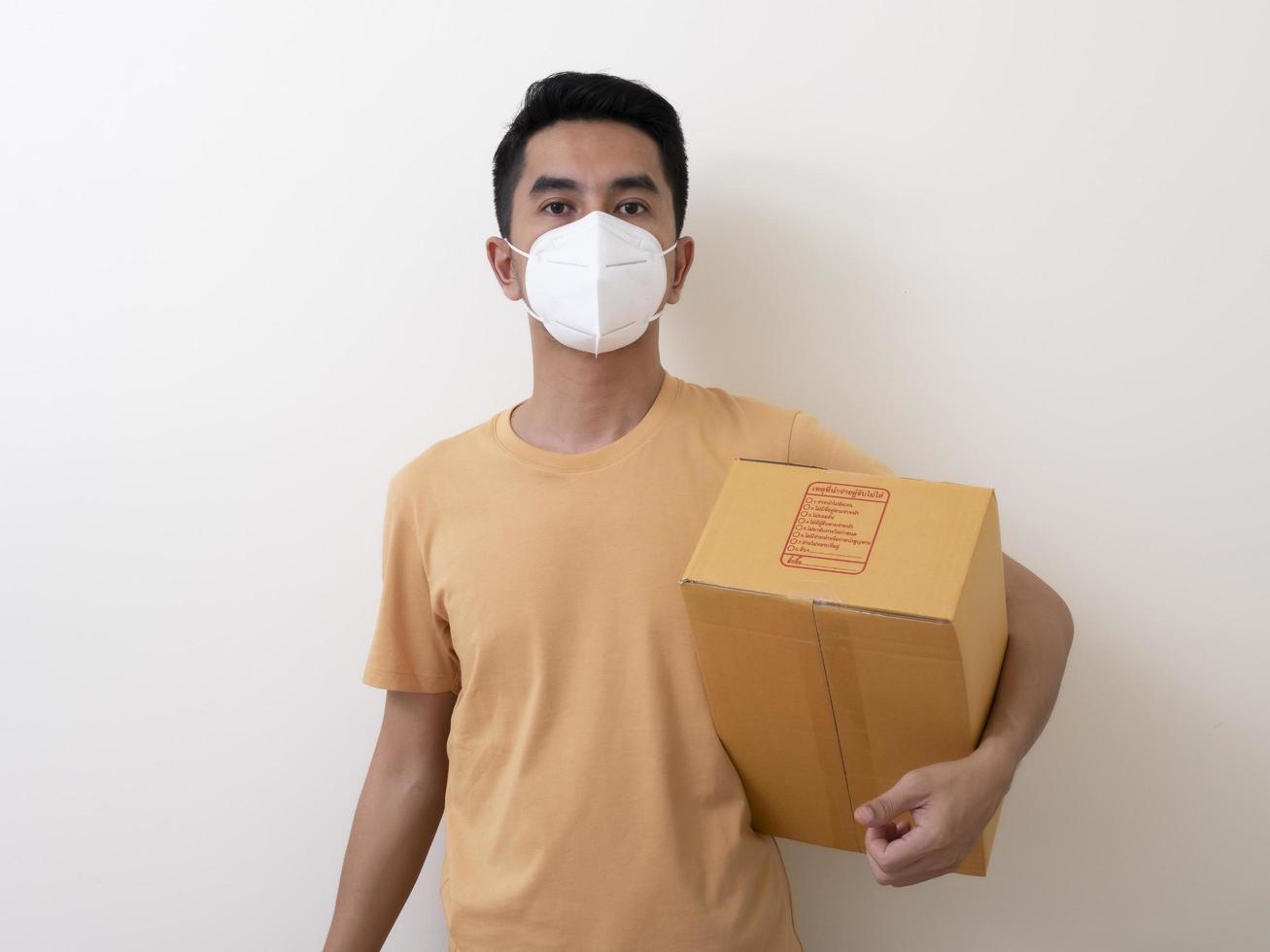 feliz empleado del servicio de entrega con mascarilla médica lleva una caja de cartón en la mano foto