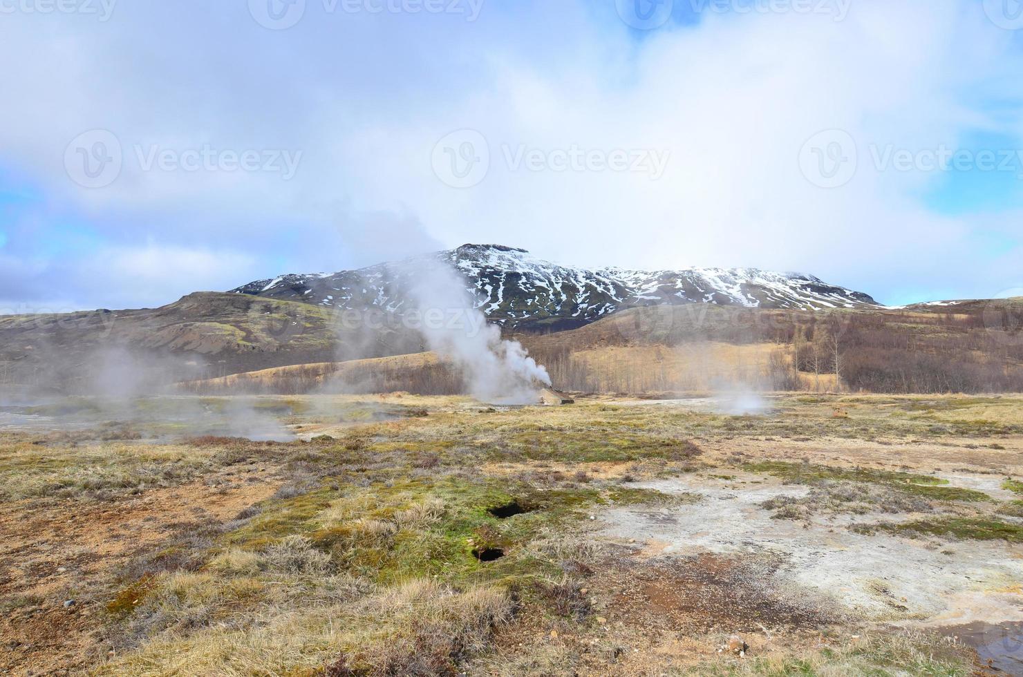 Steaming geysir with ice top mountains in the landscape photo