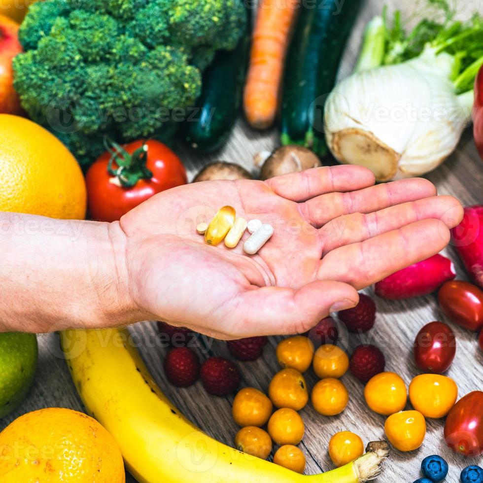 mano sujetando suplementos alimenticios sobre verduras y frutas para un estilo de vida saludable foto