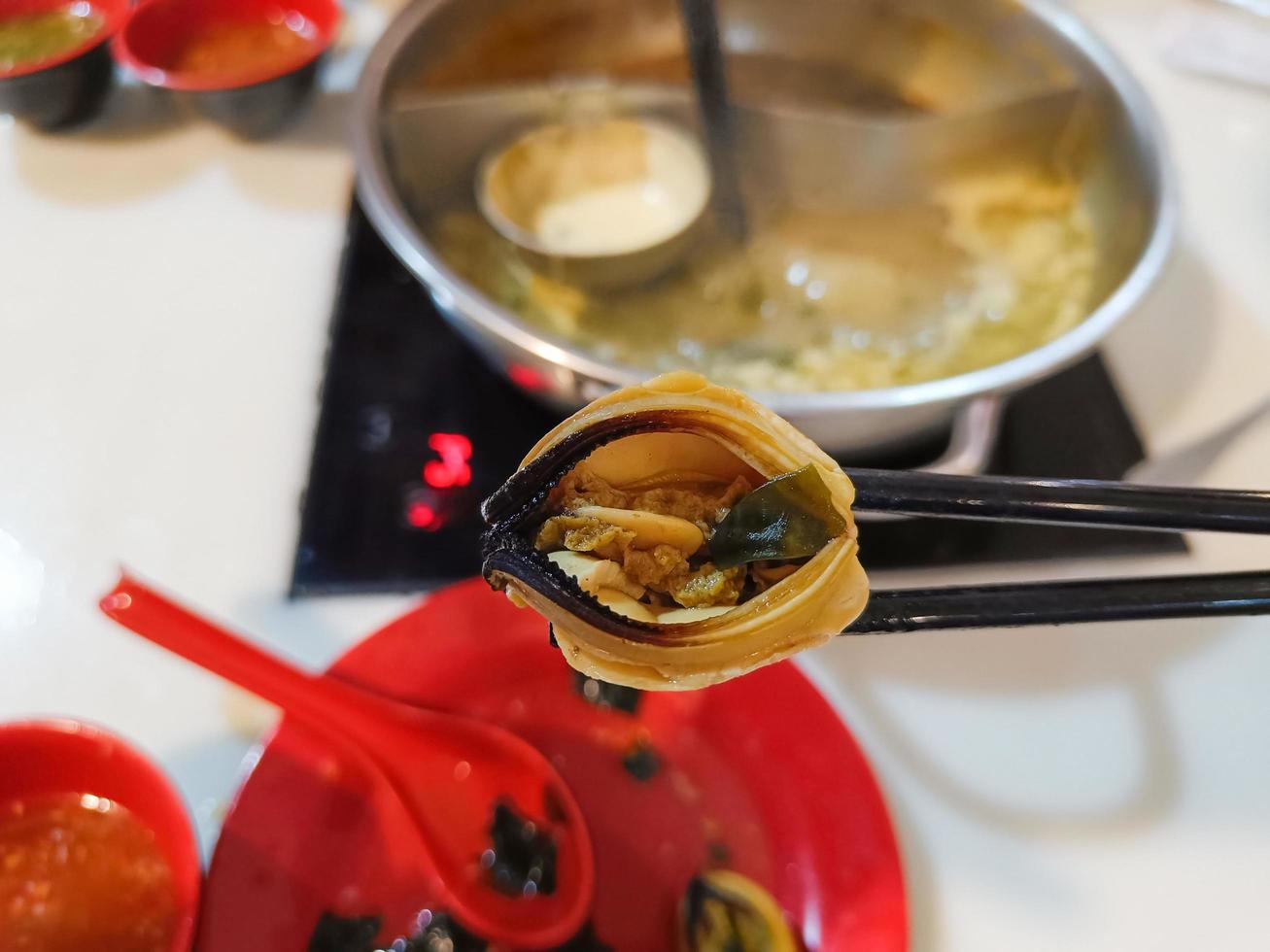 Man uses chopsticks to pick up mussels while eating a hot pot. photo