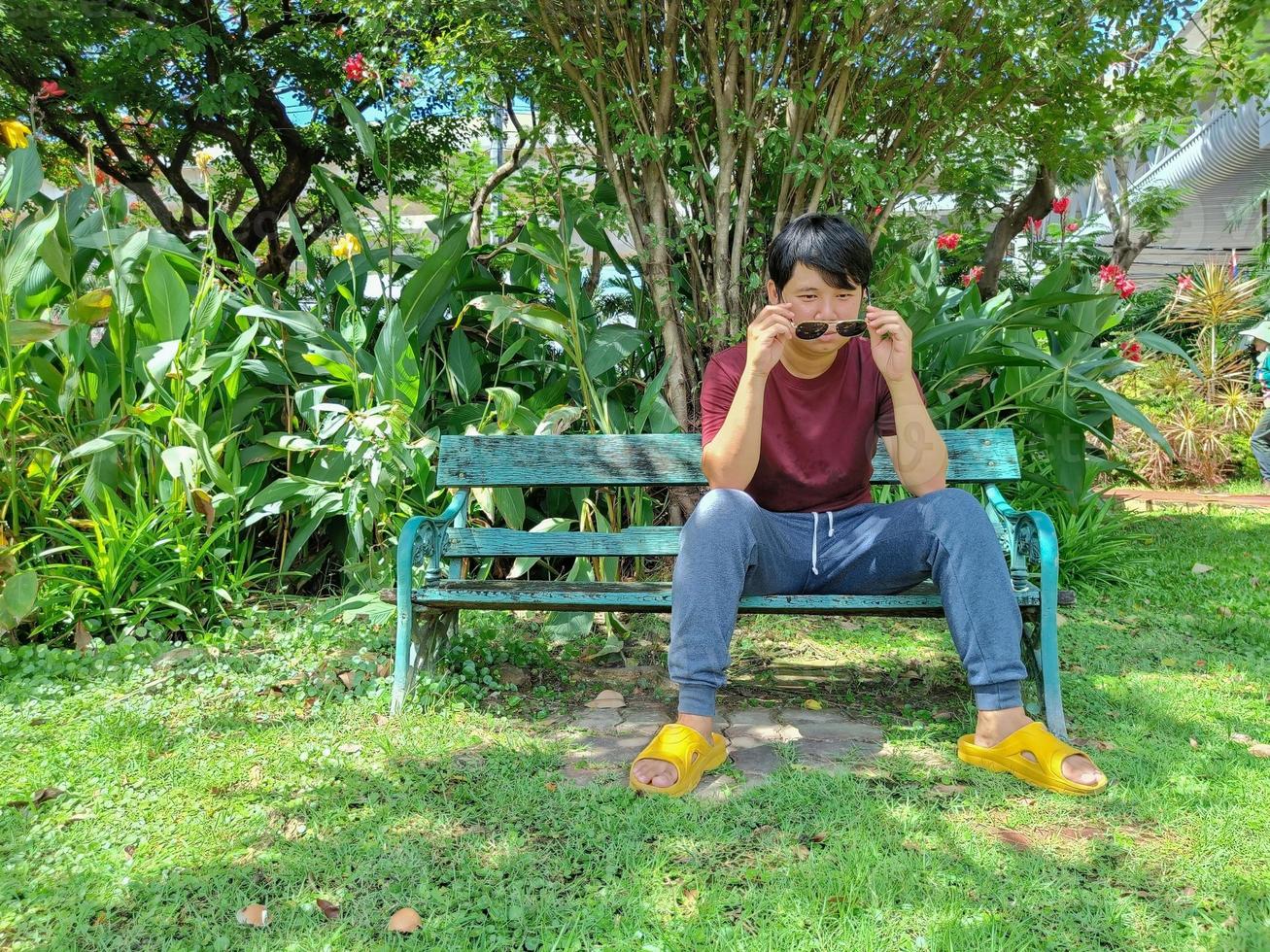 un joven asiático con el pelo negro está sentado en un banco. ¿Qué estás pensando en el parque de la ciudad? foto