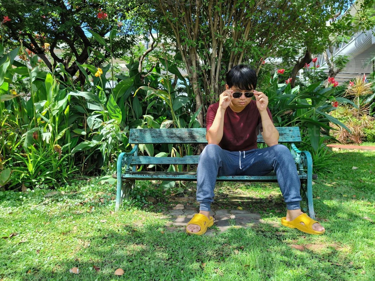 A blind Asian man with sunglasses sits alone on a bench. in the city park photo