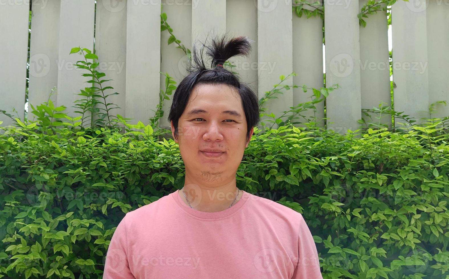 Close up of good looking bearded hipster asian guy with hair in bun, in pink shirt, happy smile, posing for photo. photo