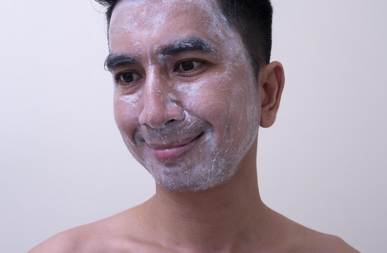 un joven apuesto asiático aplicándose crema en la cara con cara sonriente, concepto de cuidado de la piel foto