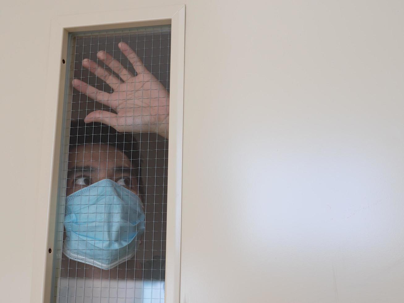 Lonely man in medical mask looking through the window. Isolation at home for self quarantine. Concept home quarantine, prevention COVID-19. Coronavirus outbreak situation photo