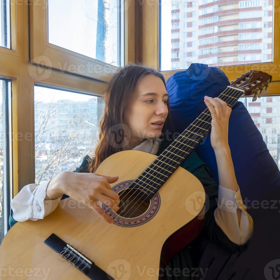 young woman playing classical guitar on the balcony photo