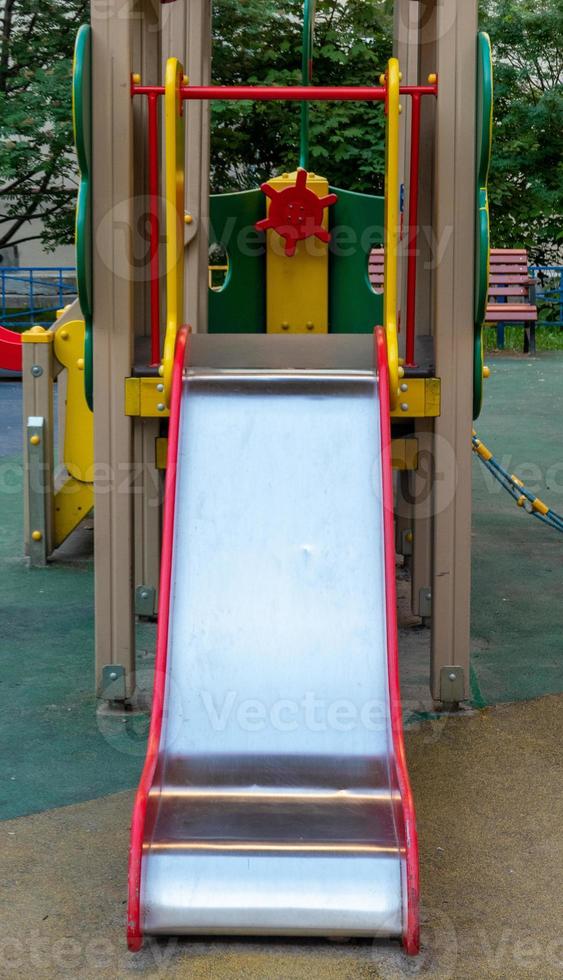 An element of a children's swing. slide. An outdoor colorful playground next to the house. A summer day. Children's playground with rubber floor covering. photo