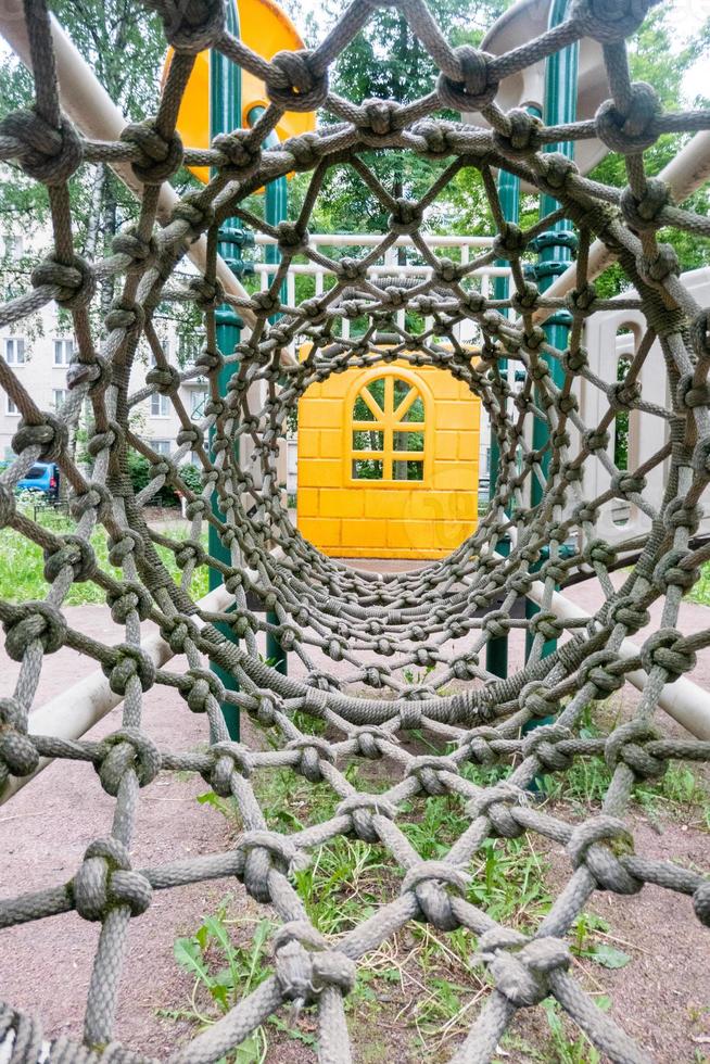 Inside view of a long rope mesh pipe, at the end of the tunnel yellow playground blurred background photo