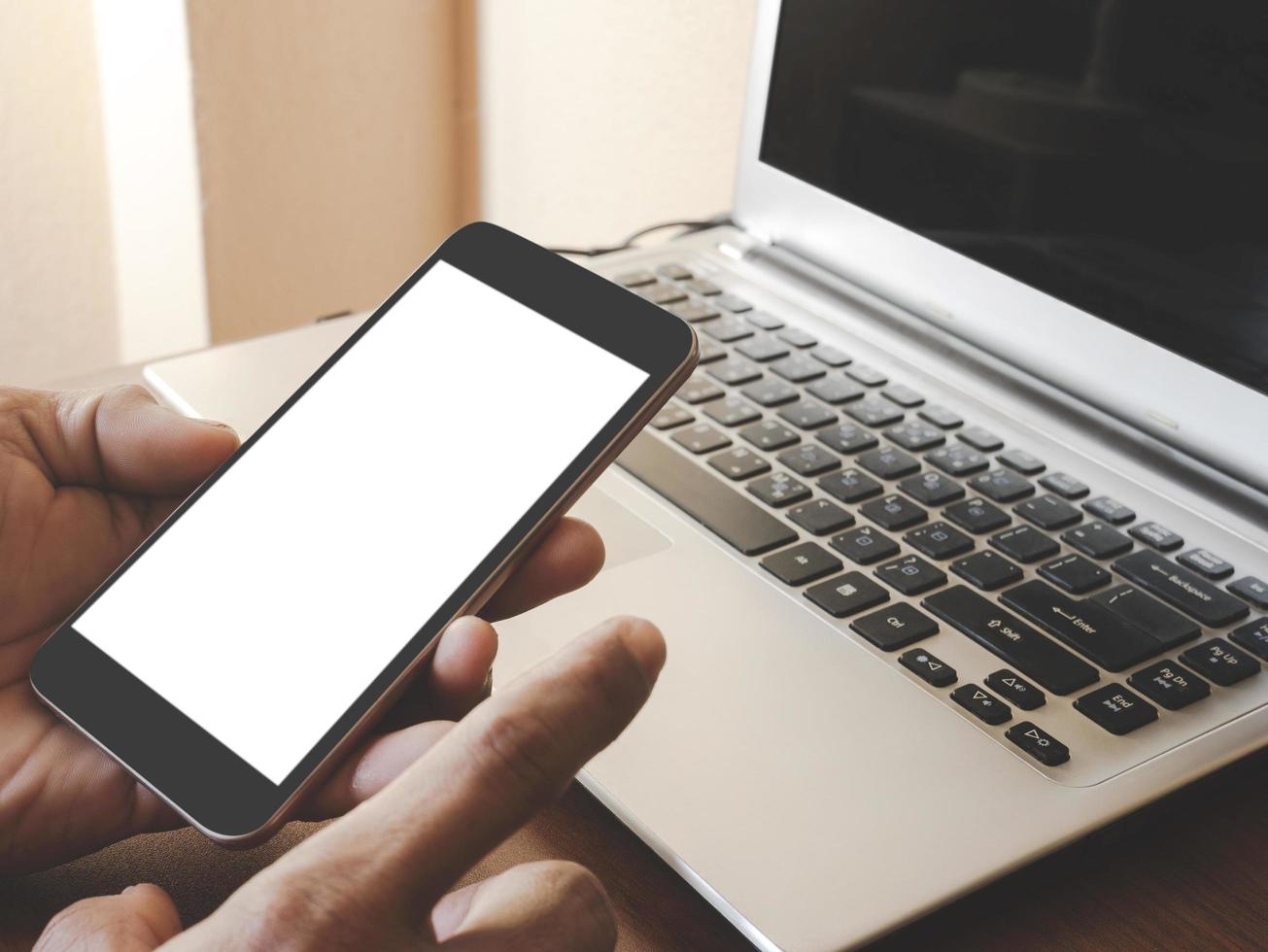 Smartphone white screen mockup on a man hand on laptop computer black keyboard white phone screen mock-up on a desk office with copy space. The concept for using an advertising banner text. photo