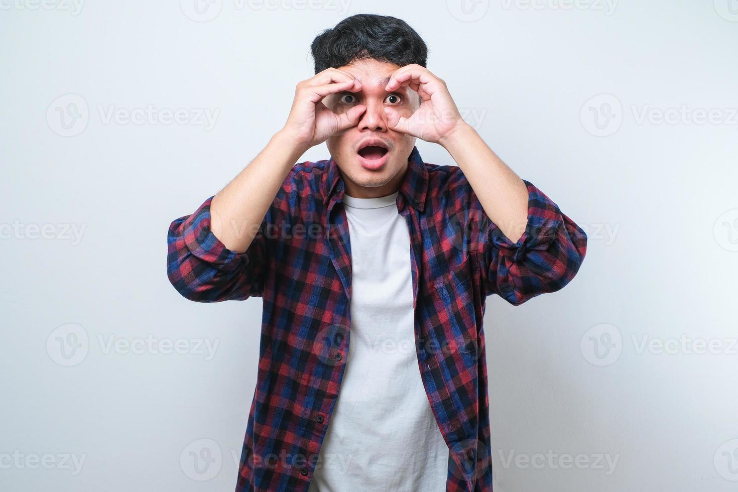 Young handsome man wearing casual shirt doing ok gesture like binoculars sticking tongue out, eyes looking through fingers. photo