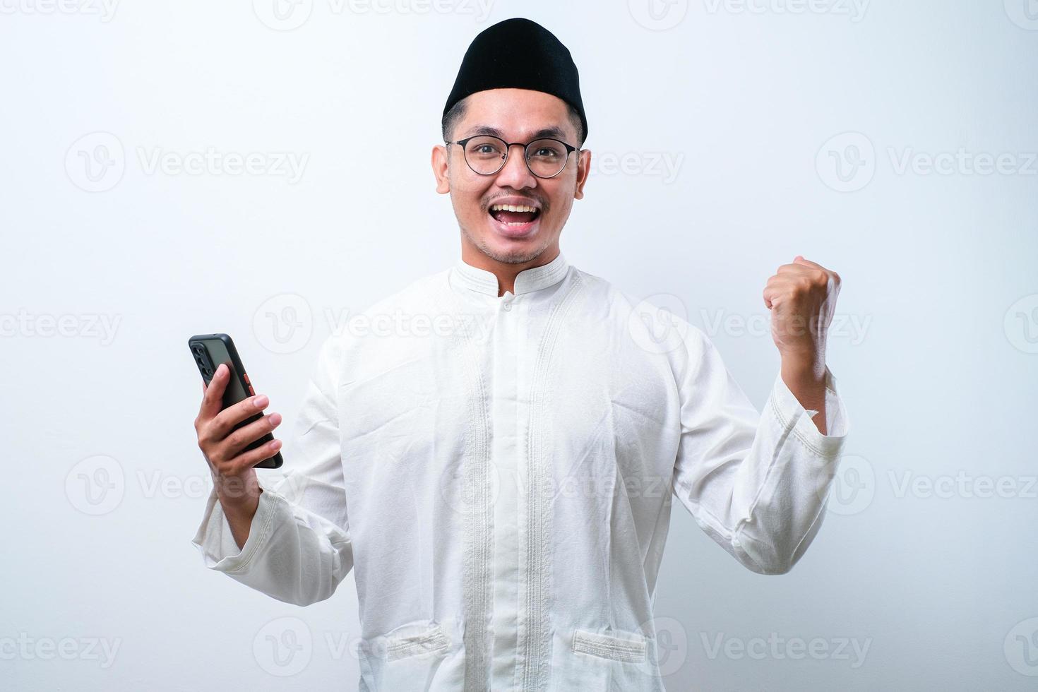 Asian muslim man holding smartphone doing winning gesture holding mobile phone, Happy get special gift online photo