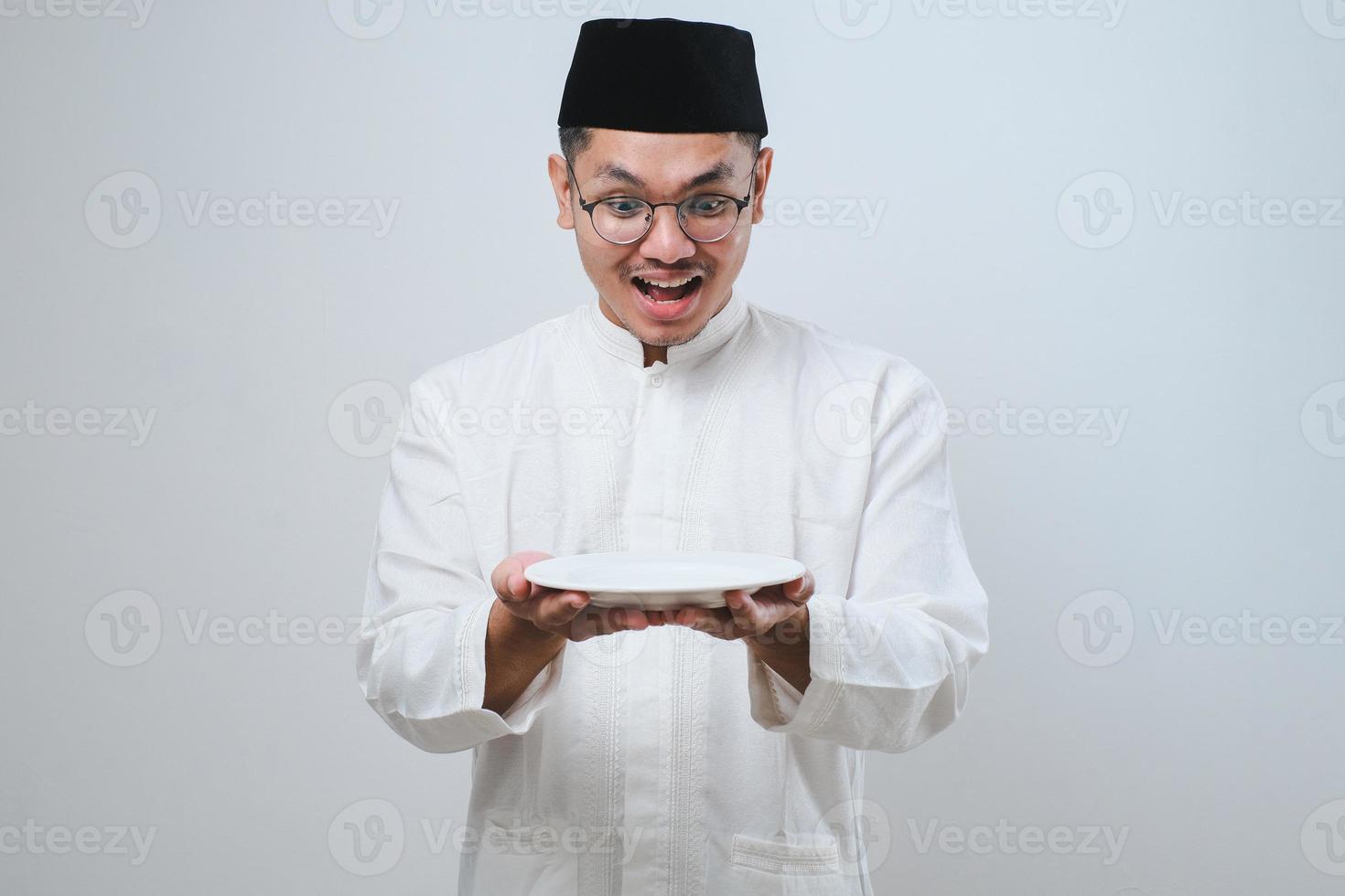 Asian muslim man showing excited expression while holding empty dinner plate photo