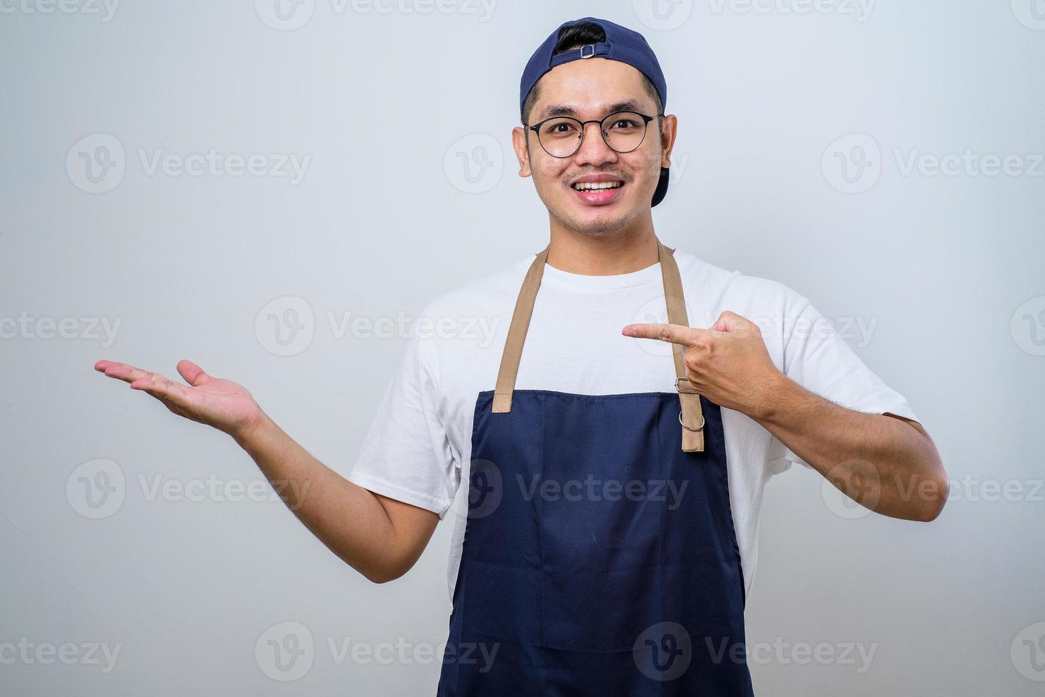 Young handsome asian barista man wearing apron showing product, pointing at something with hands. photo