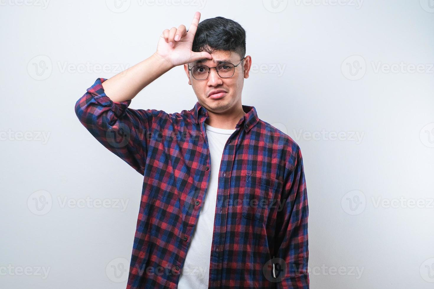 Young handsome man making fun of people with fingers on forehead doing loser gesture mocking and insulting. photo