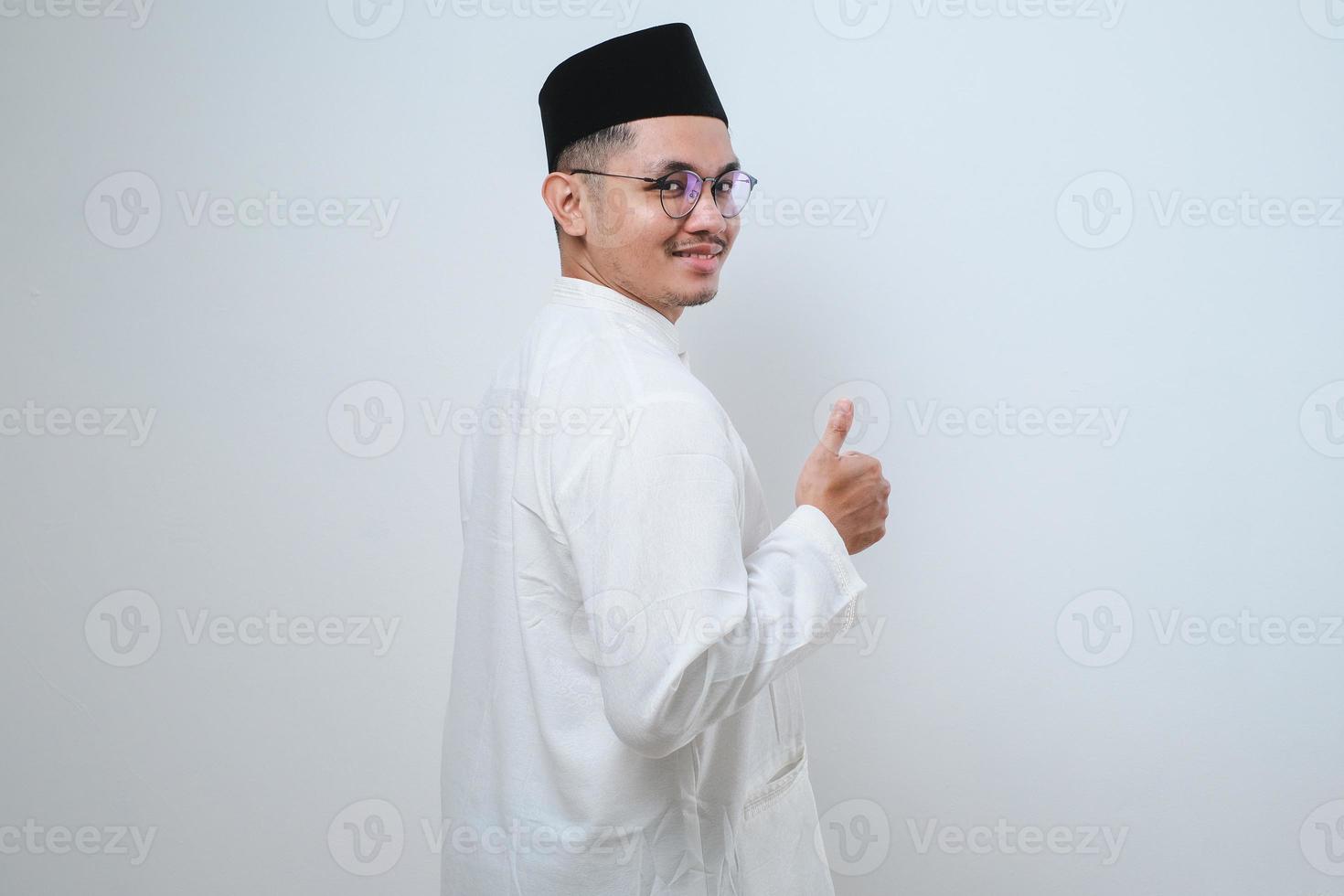 Handsome Young Asian Muslim man showing thumb up to copy space, looking at camera. photo