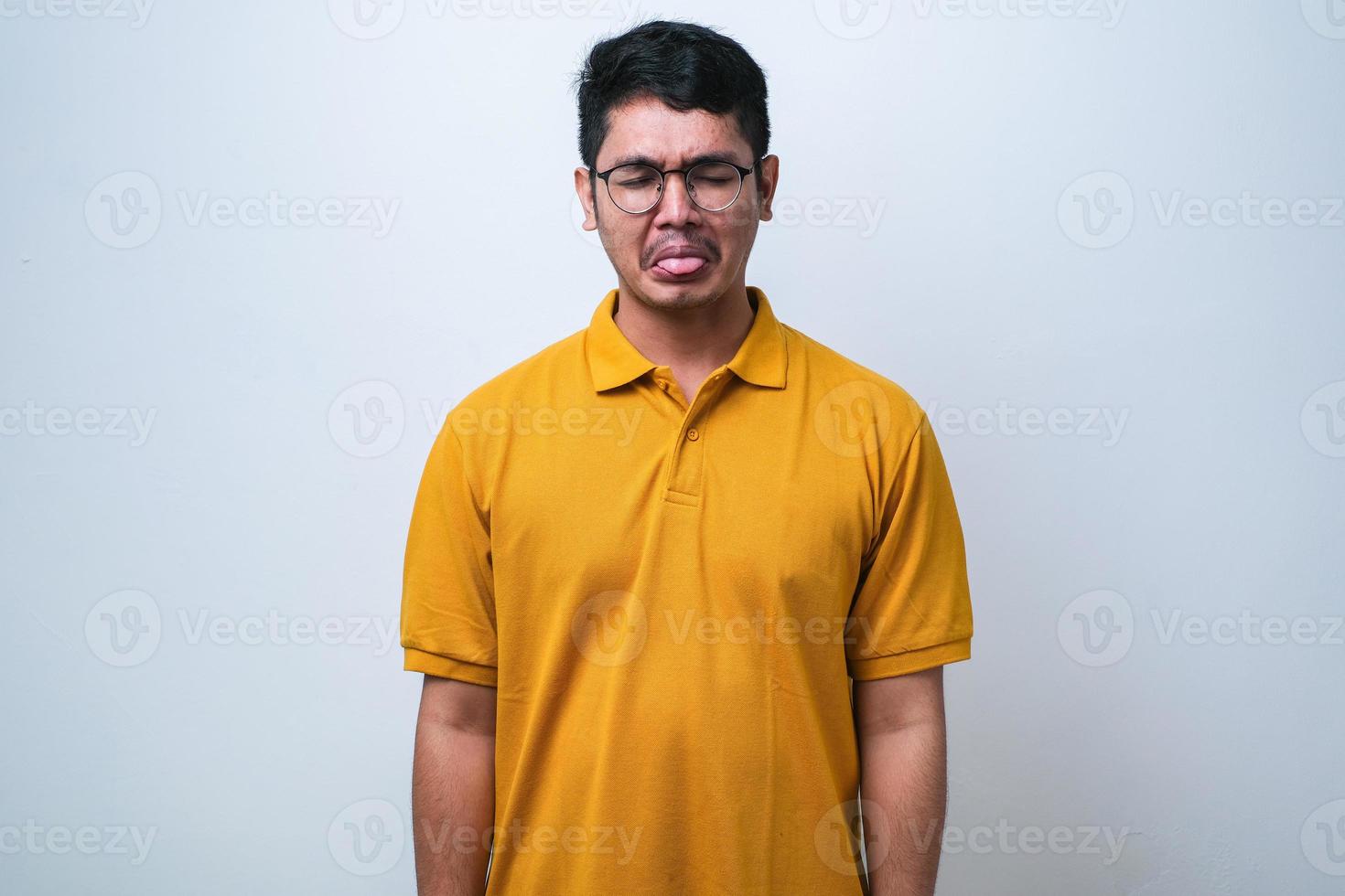 joven y apuesto chico asiático con pantalones casual sobre fondo blanco sacando la lengua feliz con una expresión graciosa. foto