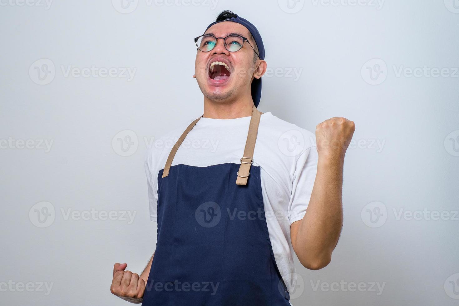 Asian barista man wearing apron standing very happy and excited doing winner gesture with arms raised, smiling and screaming for success. Celebration concept. photo