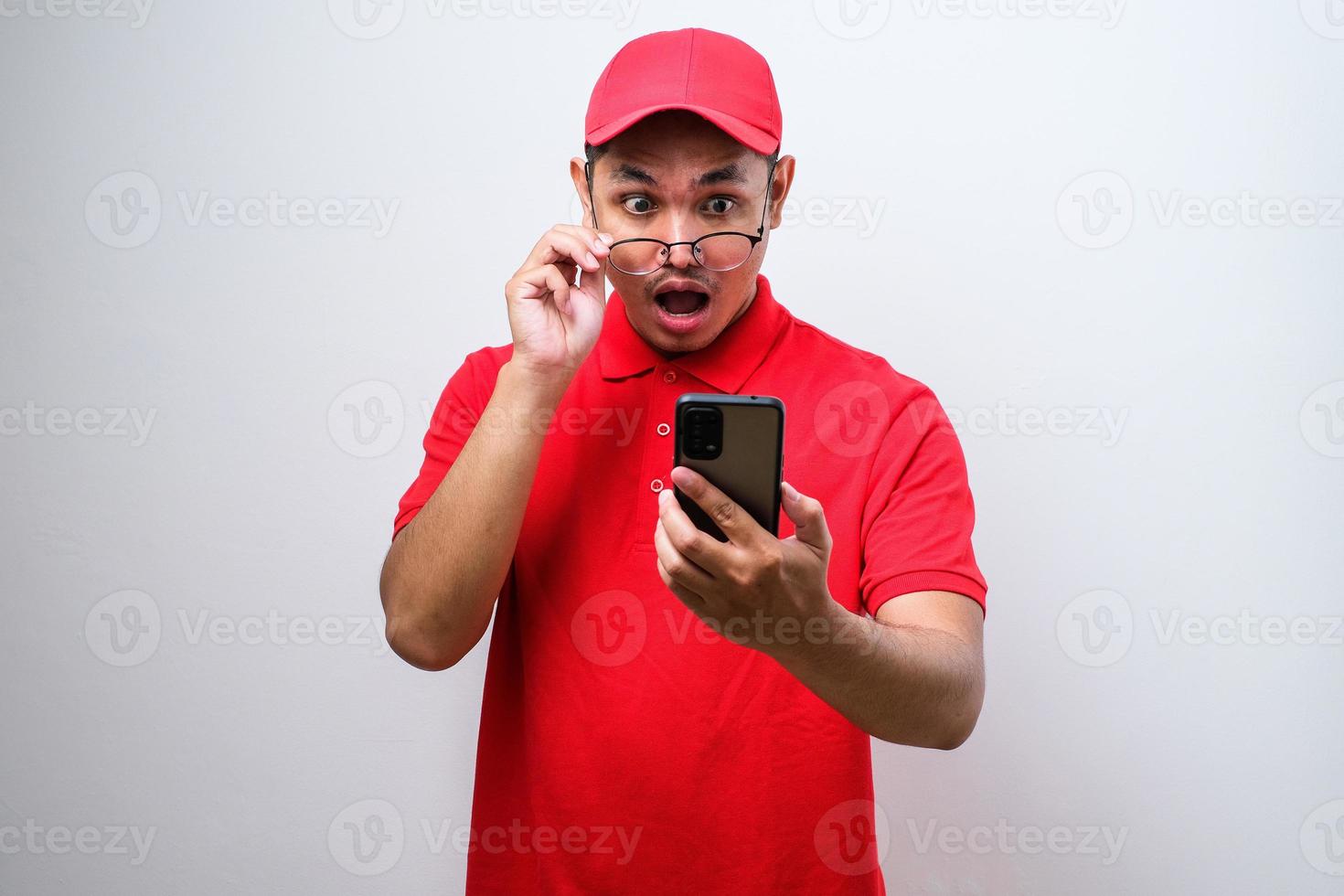 Asian delivery man wearing red shirt looks surprised at the good news he received from his smartphone. photo