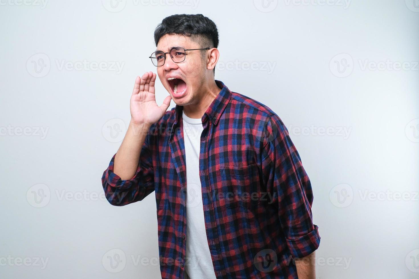 Young asian man shouting and screaming loud to side with hand on mouth photo