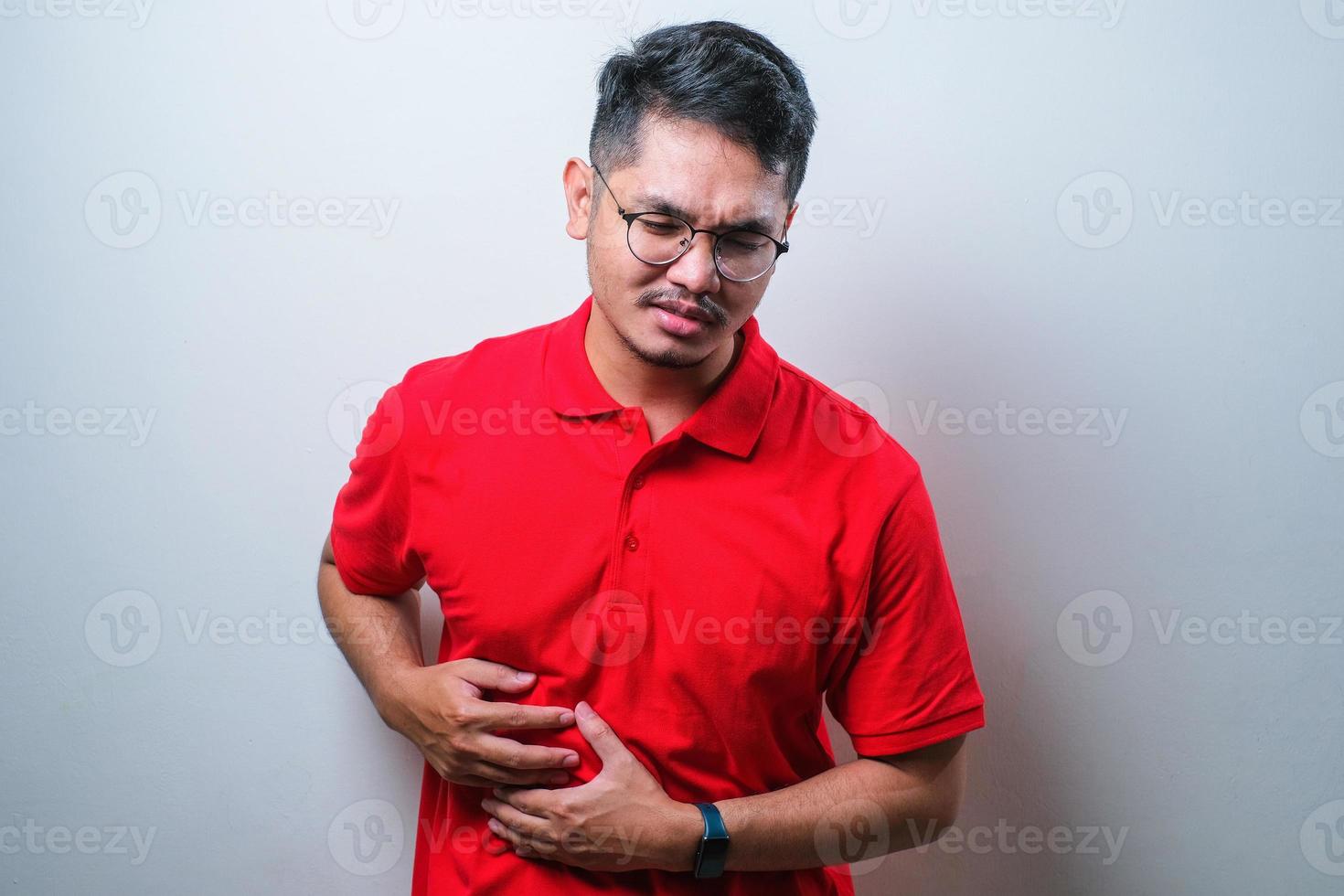 Young handsome Asian man with hand on stomach because nausea, painful disease feeling unwell. Ache concept. photo