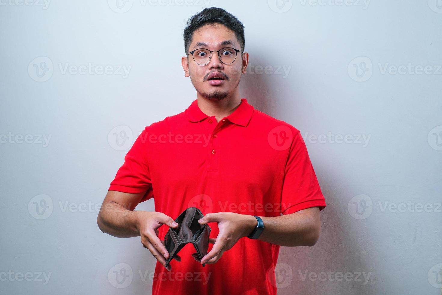 Young handsome Asian man wearing casual shirt showing empty wallet with shocked face expression, surprised and speechless photo