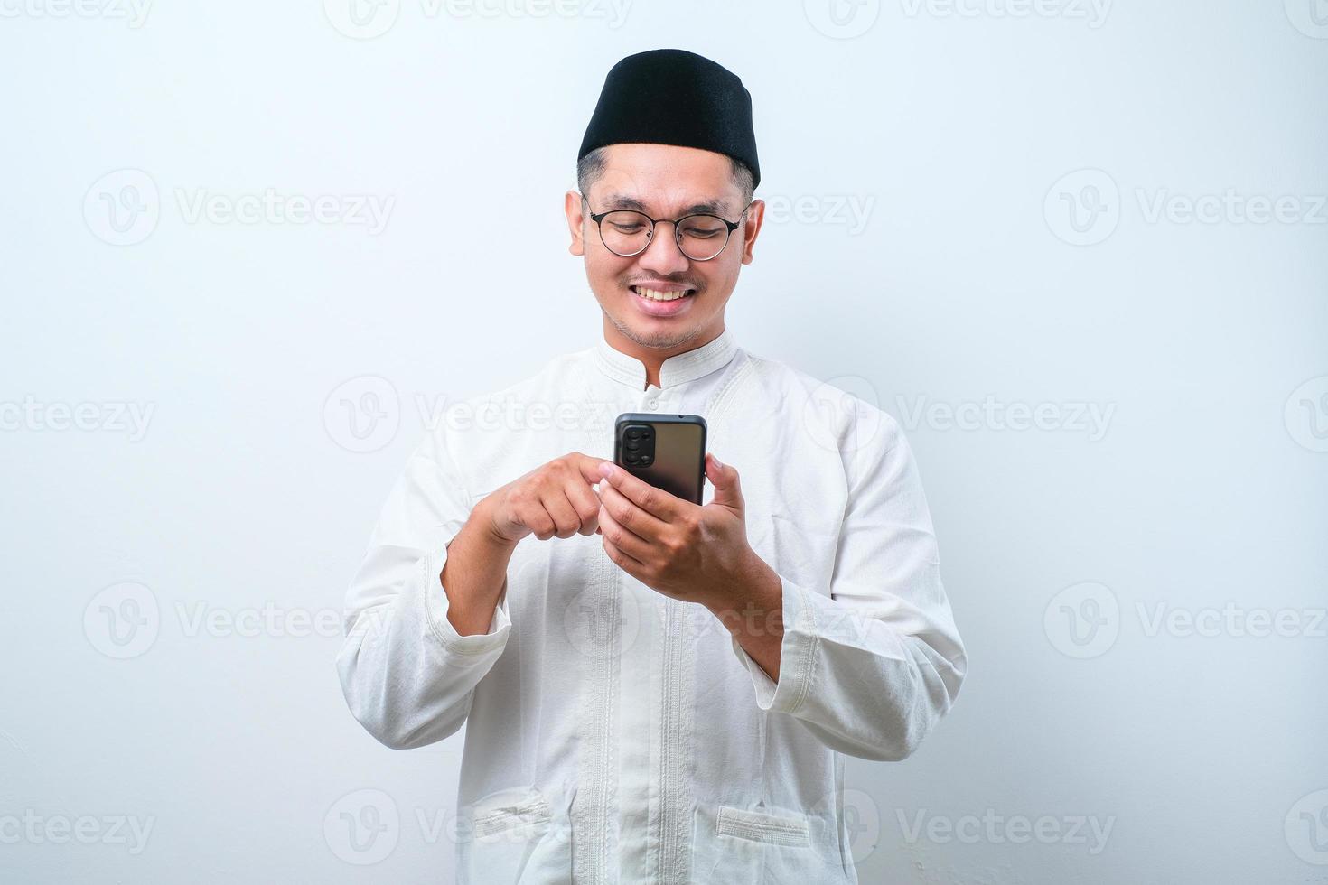 Happy asian muslim man holding and pointing on phone cellular over white background photo