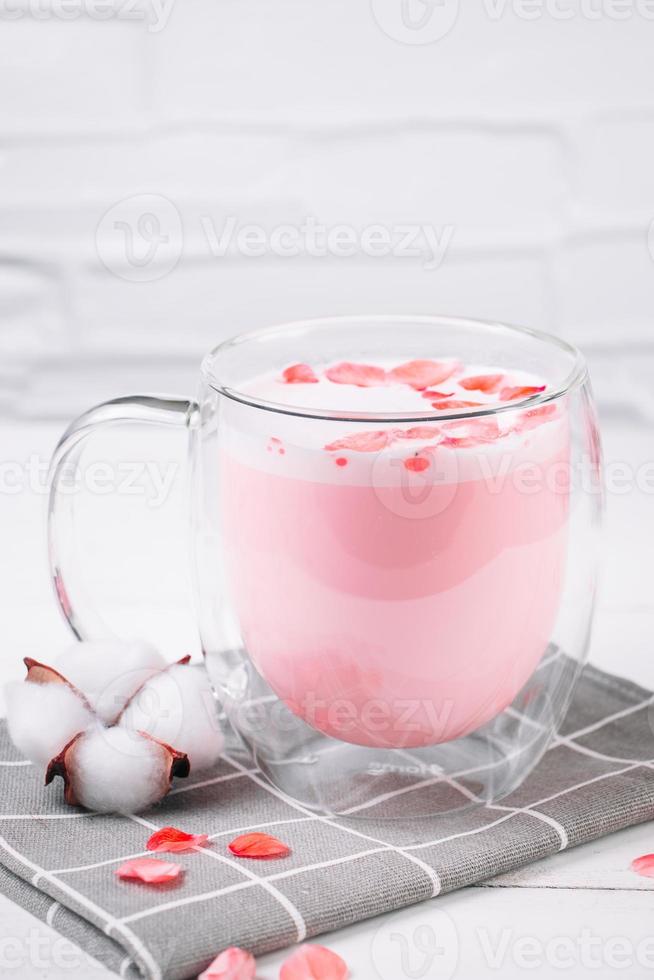 Pink matcha with rose petals on white background. Transparent cup with trendy vegan whipped tea. Moon milk. Relaxing drink for sleepy time. photo