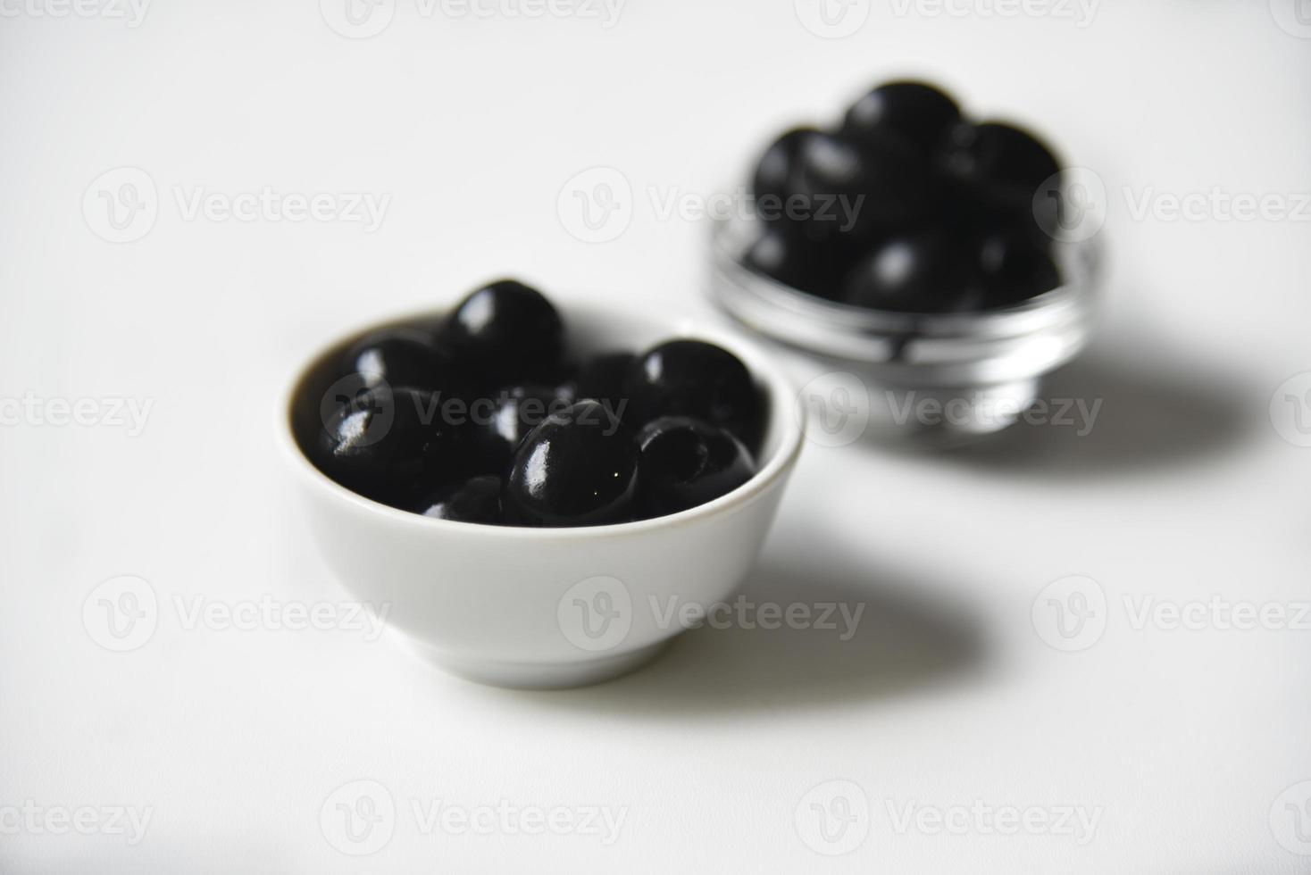Black olives in a white and glass saucepan on a white background. photo