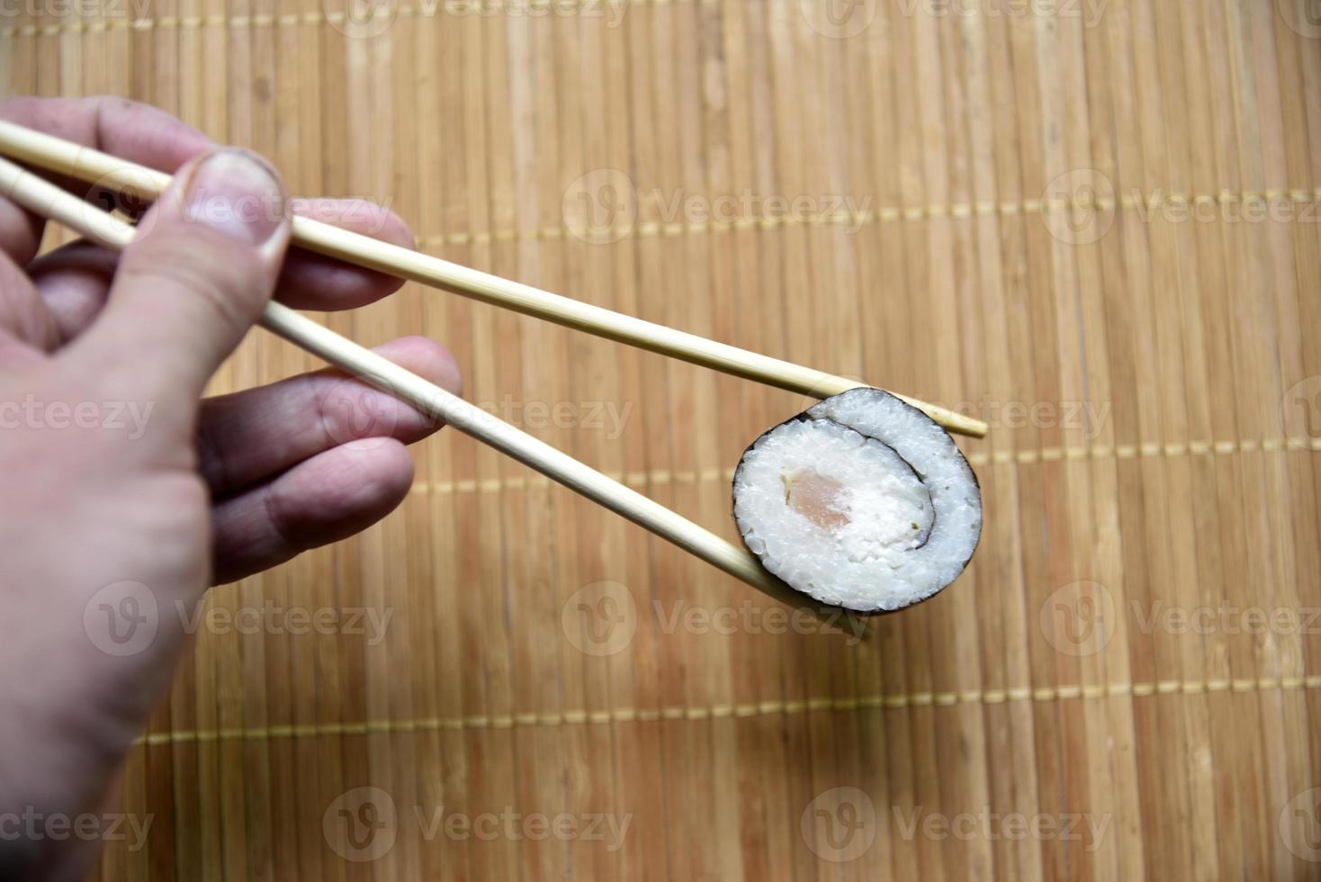 Taken with chopsticks sushi with tuna for eating. Delicious fish roll. Rice sushi roll on a mat. photo