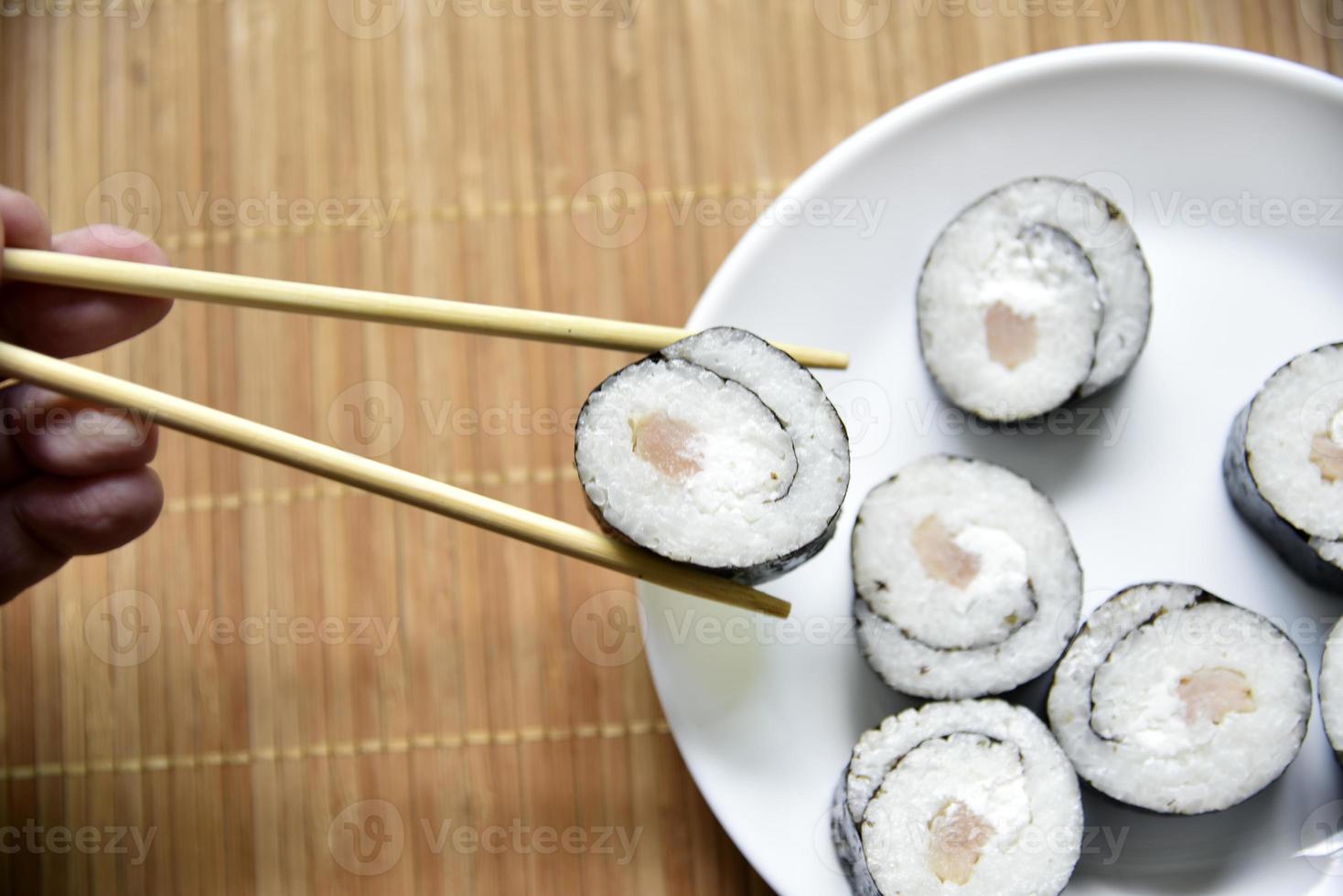 Taken with chopsticks sushi with tuna for eating. Delicious fish roll. Rice sushi roll on a mat. photo