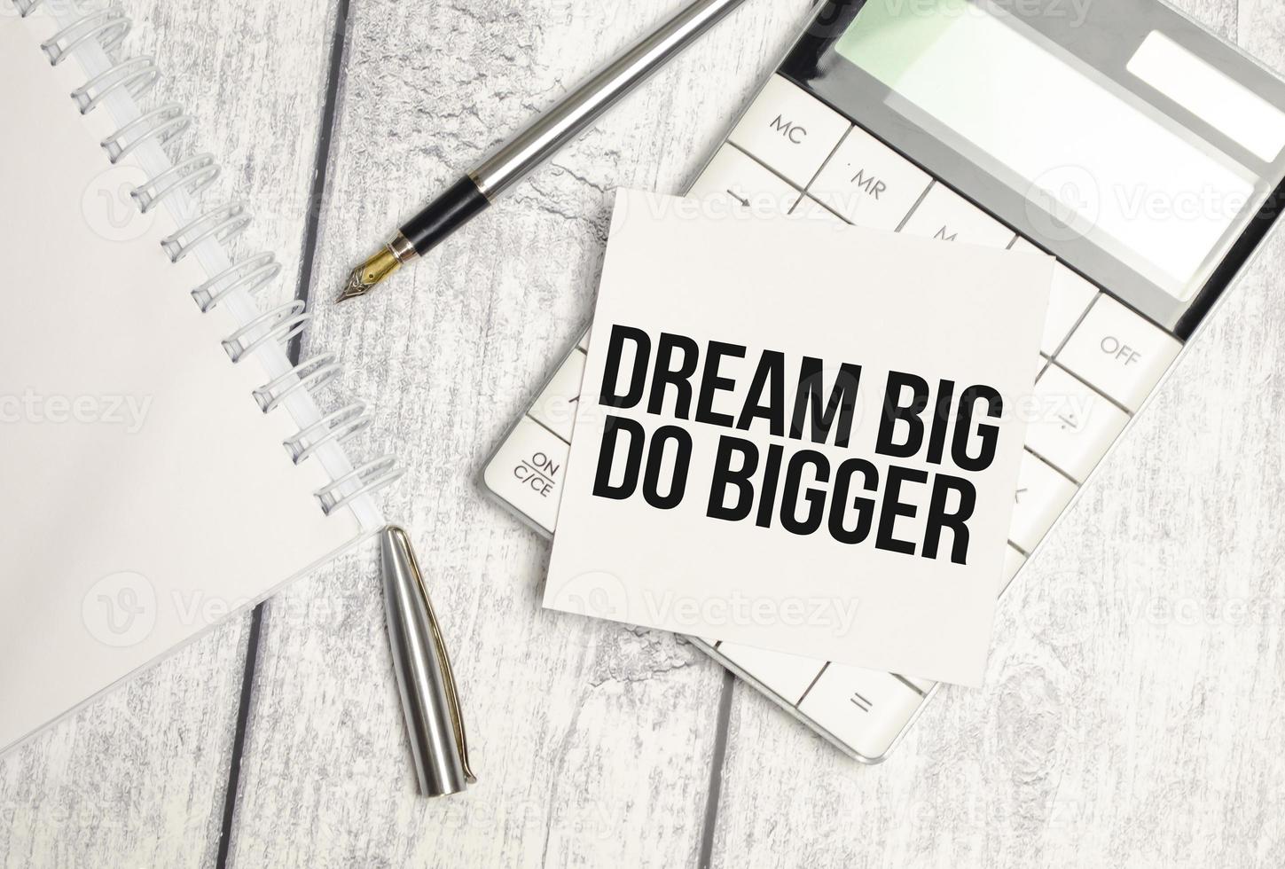 Text Think Big Do Bigger on paper card and calculator on wooden background photo