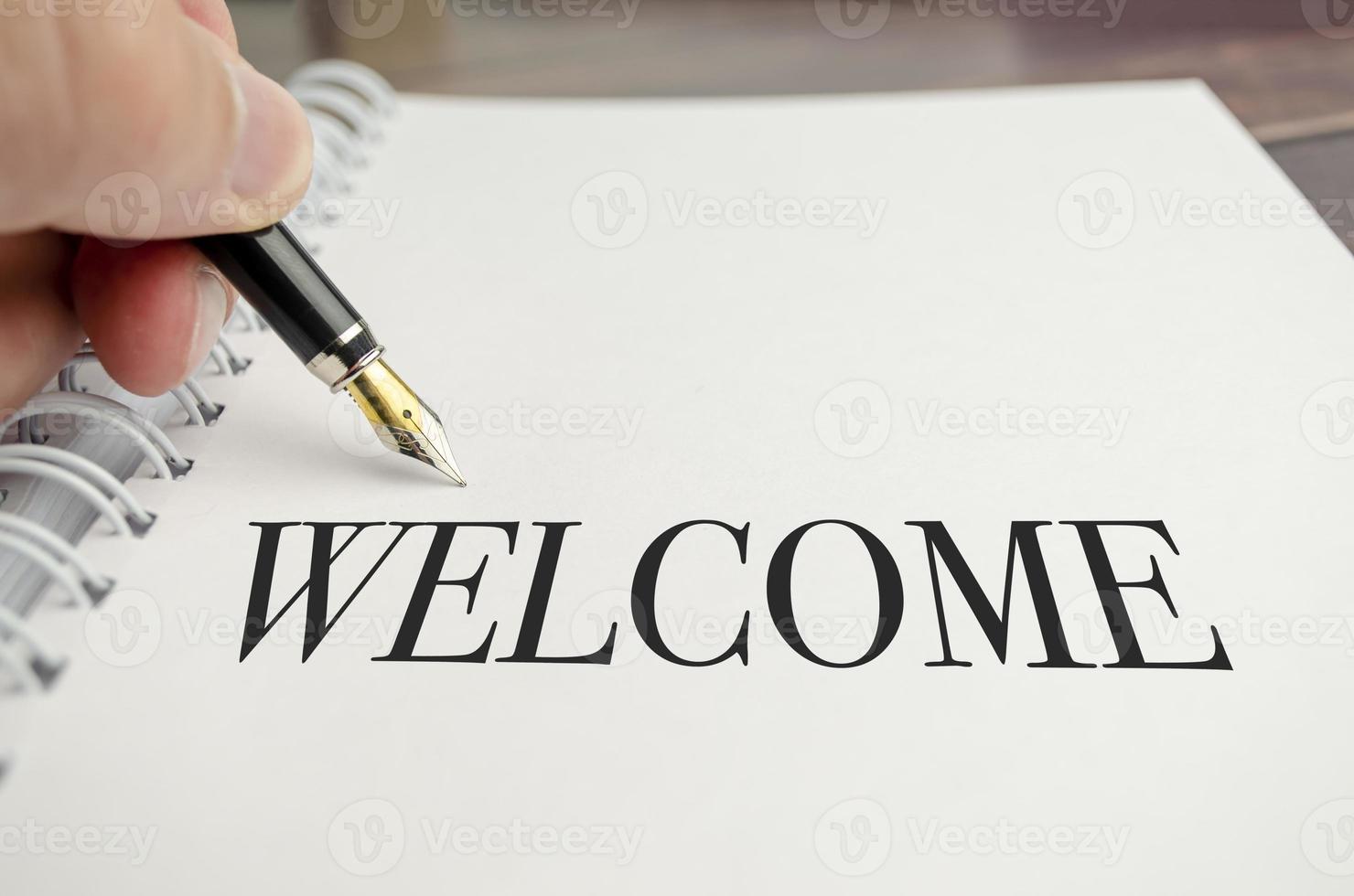 hand writing welcome on white notepad on wooden background photo