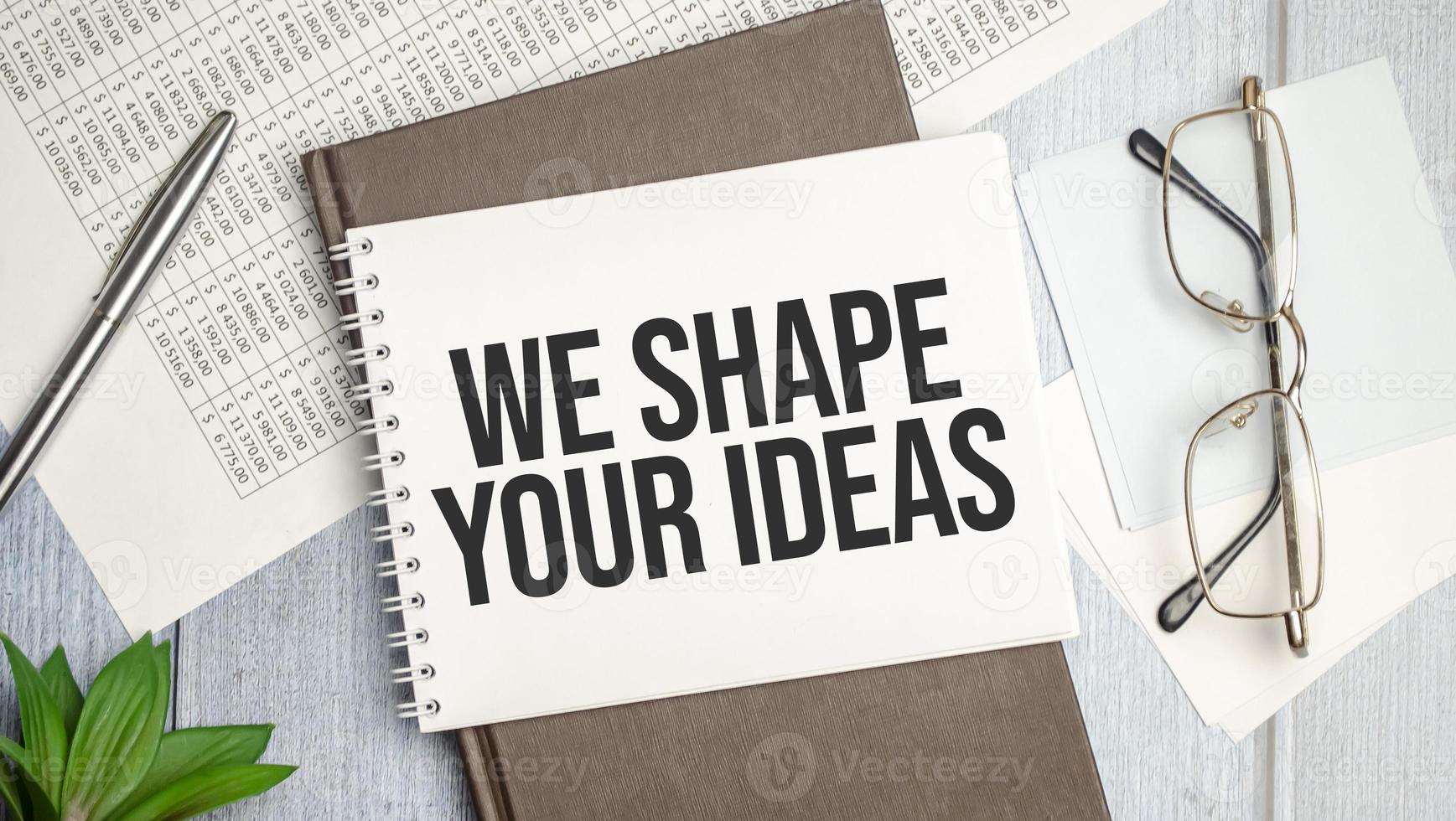 we shape your ideas text on notepad with glasses, pen and charts photo