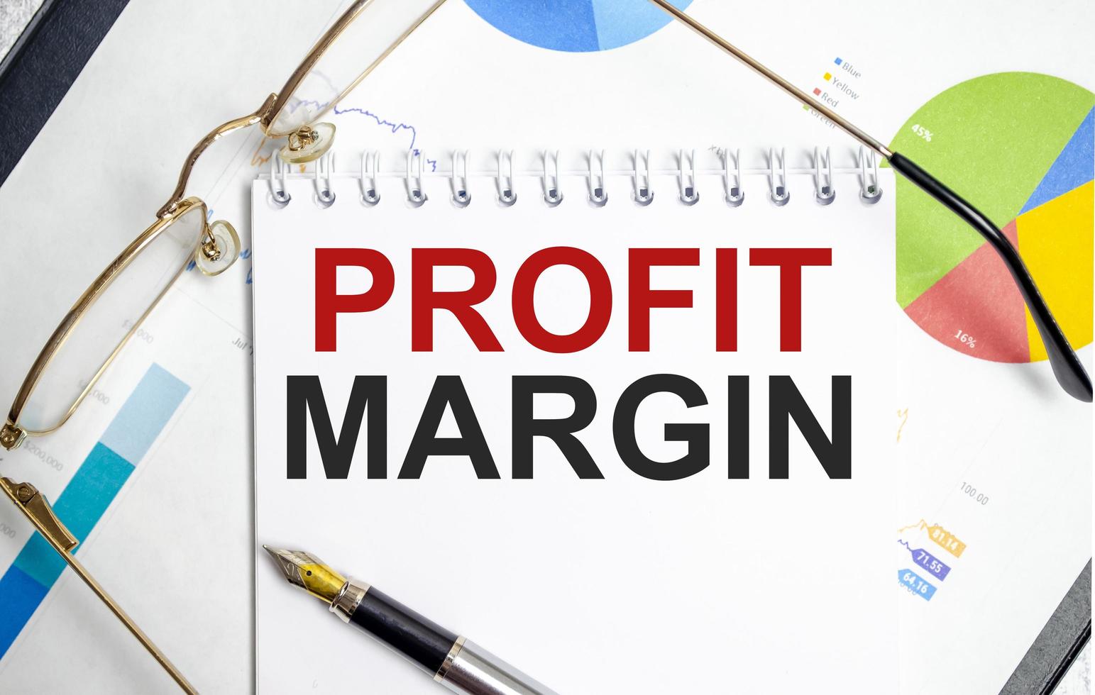 PROFIT MARGIN word on notepad with glasses and chart photo