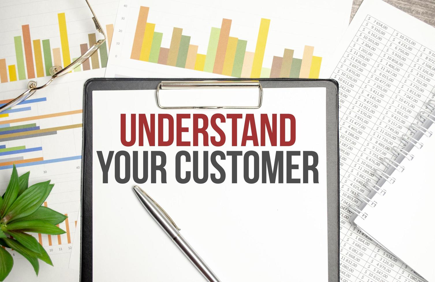 Paper with UNDERSTAND YOUR CUSTOMER on a table with charts, glasses and pen photo