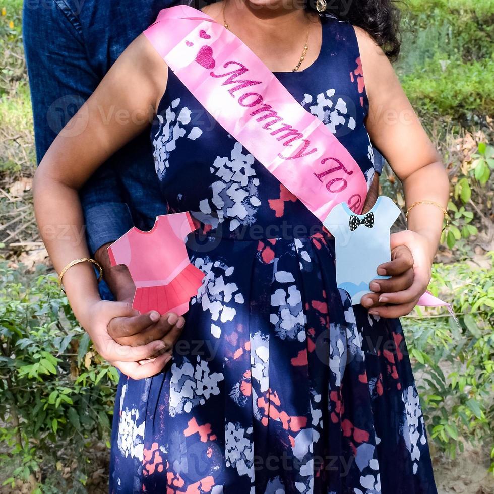 Indian couple posing for maternity baby shoot. The couple is posing in a lawn with green grass and the woman is falunting her baby bump in Lodhi Garden in New Delhi, India photo