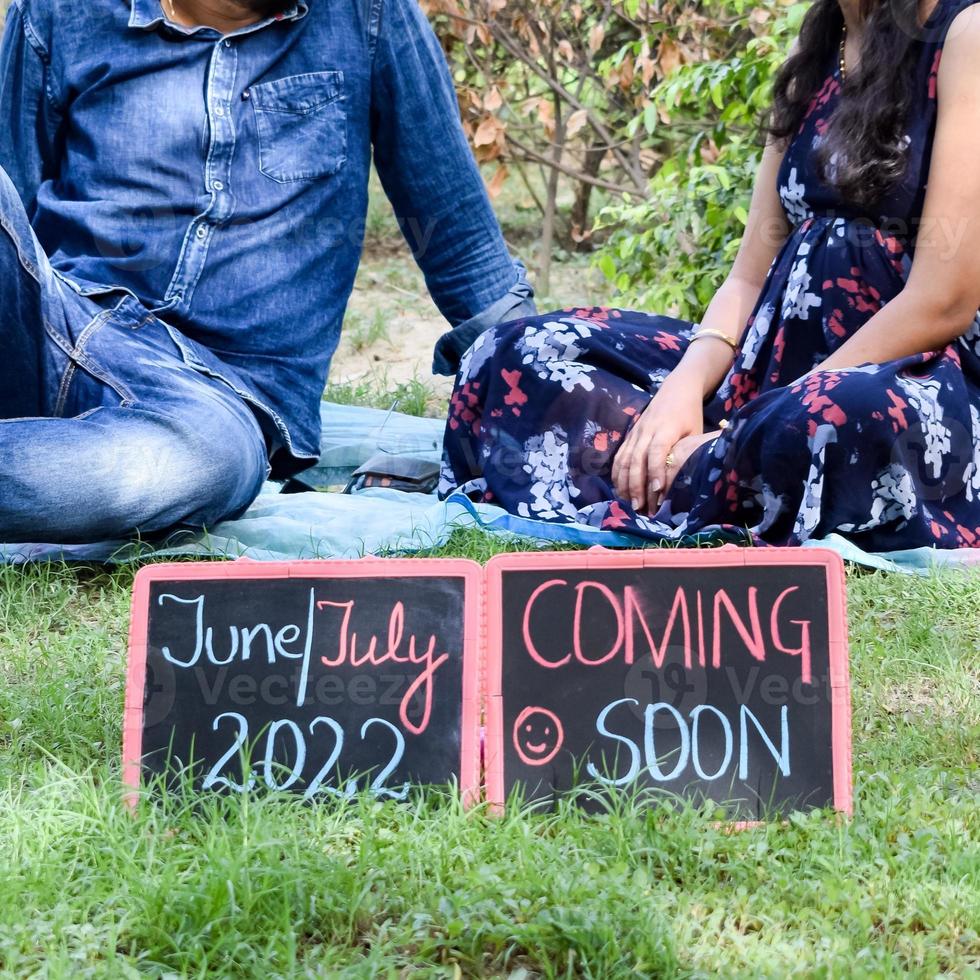 Indian couple posing for maternity baby shoot. The couple is posing in a lawn with green grass and the woman is falunting her baby bump in Lodhi Garden in New Delhi, India photo